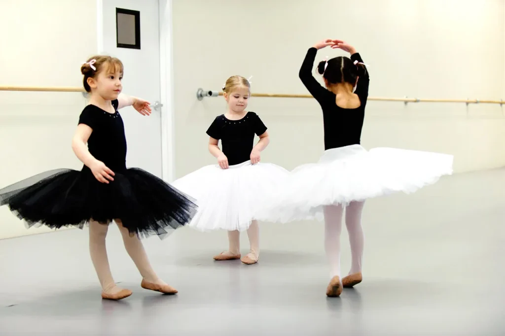 Three toddler ballet students in a studio wearing white and black tutus