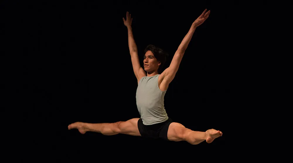 Male dancer in center split jump arms in high v
